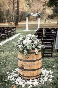 a wooden barrel with white flowers on the grass near rows of chairs and an aisle