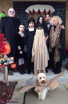 a group of people dressed up in costumes standing on the front porch with a dog