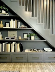 a bookshelf under the stairs is filled with books and vases on it