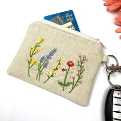 a small purse with flowers on it next to a cell phone and flower keychain