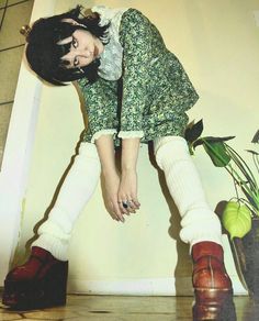 a woman in green dress sitting on top of a wooden floor next to a potted plant