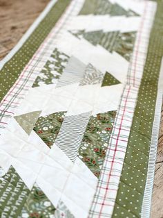 a quilted table runner with green and white christmas tree designs on it, sitting on a wooden surface