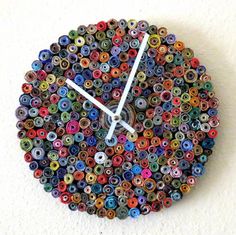 a multicolored clock made out of rolled up magazines on a white wall with yellow hands