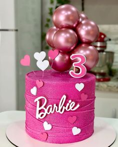 a pink cake topped with lots of balloons and the number three on it's top