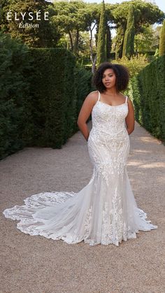 a woman in a white wedding dress standing on a path surrounded by bushes and trees