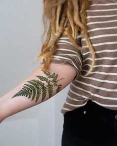 a woman's arm with a fern tattoo on it