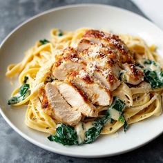 a white plate topped with pasta covered in chicken and spinach sauce on top of a table