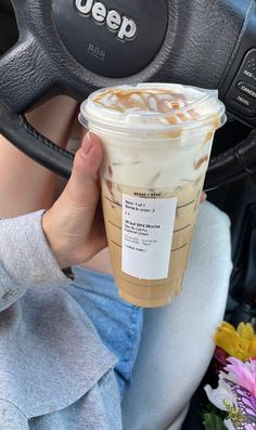 a woman holding up a cup of coffee in her hand while sitting in a car