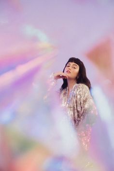 a woman standing in front of a colorful background with her hand on her chin and looking up