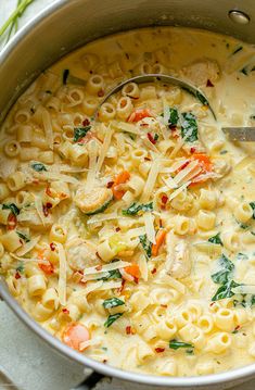 a pot filled with pasta and vegetables on top of a table next to a spoon