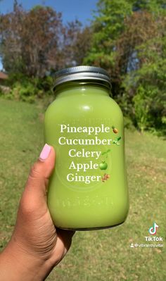 a hand holding a green glass jar with pineapple cucumber celery apple ginger on it