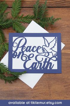 a card with the words peace and earth on it, surrounded by evergreen branches in blue ink