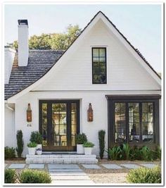 a white house with black doors and windows in the front yard is surrounded by greenery