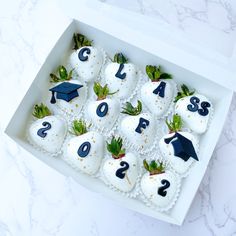 a box filled with white chocolate covered in frosting and topped with strawberries, green leaves and graduation caps