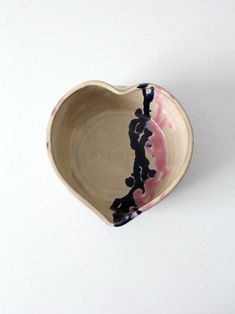 a small heart shaped bowl with black and pink designs on the outside, sitting on a white surface