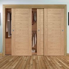 an open wooden closet with clothes hanging on the doors and wood flooring in front of it