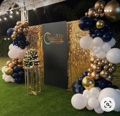 an outdoor event with balloons and decorations on the grass in front of a gold wall