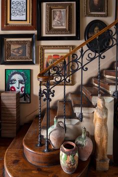 there are many framed pictures on the wall behind this stair case, along with vases and urns