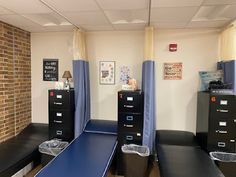 an office with black file cabinets and blue drapes on the window sill, in front of a brick wall