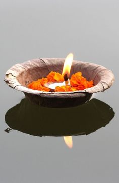 a small bowl filled with orange flowers floating on top of a body of water next to a lit candle