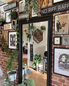 a brick wall covered in lots of framed pictures and plants next to potted plants