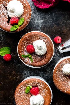 three chocolate desserts with whipped cream and raspberries on top, one topped with powdered sugar