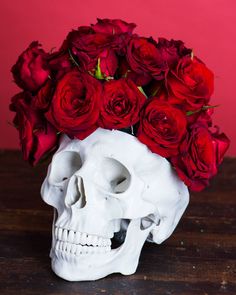 a skull with roses in it's head sitting on a wooden table next to a red wall