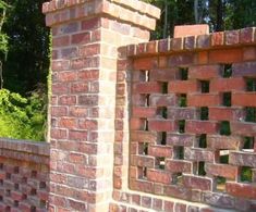 a red brick wall with holes in the middle and trees in the backround