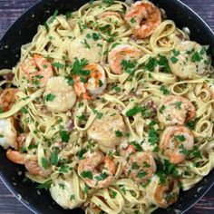 pasta with shrimp and parsley in a skillet on a wooden table, ready to be eaten