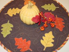 a decorative table mat with a pumpkin and autumn leaves on it, along with berries