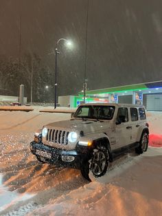 a jeep is driving through the snow in front of a gas station on a snowy night