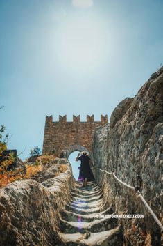 a person walking up some stairs in front of a stone wall with an arch over it