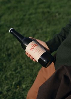 a person holding a bottle of wine in their hand while sitting on the grass outside