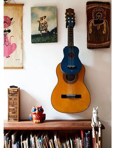 a guitar hanging on the wall next to a book shelf with books and other items