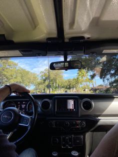 a person driving a car with the sun shining through the windshield and trees in the background