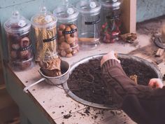 a person is scooping dirt into a bowl on a table with jars and other items