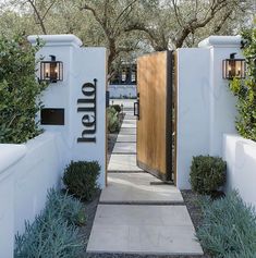 an entrance to a home with white walls and wooden doors, surrounded by greenery