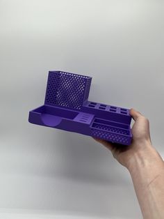 a hand holding a purple plastic object with holes in the middle and bottom section,