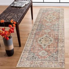 a large rug is on the floor next to a bench and vase with flowers in it