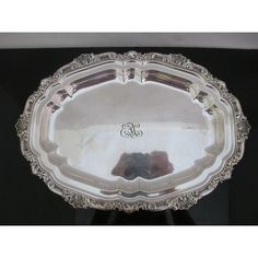 an ornate silver plate with monogrammed initials on the bottom and sides is displayed against a black background