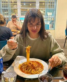 a woman sitting at a table in front of a plate of food with spaghetti on it