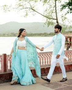 a man and woman holding hands while standing next to each other in front of a body of water