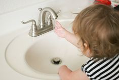 a toddler playing with the faucet in the bathroom sink