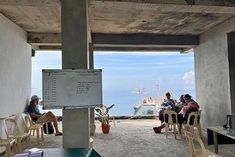 people sitting at tables in an open area near the ocean