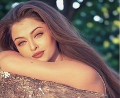 a woman with long hair leaning on a tree trunk