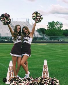 two cheerleaders standing on top of cones in the middle of a football field