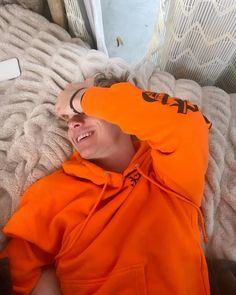 a man in an orange hoodie laying on top of a bed