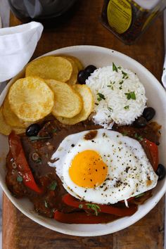 a bowl filled with rice, beans and an egg next to potato wedges on a cutting board