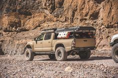 two trucks parked next to each other in front of a rocky mountain side with rocks on the ground