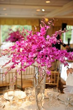 a tall vase filled with purple flowers on top of a white table cloth covered table